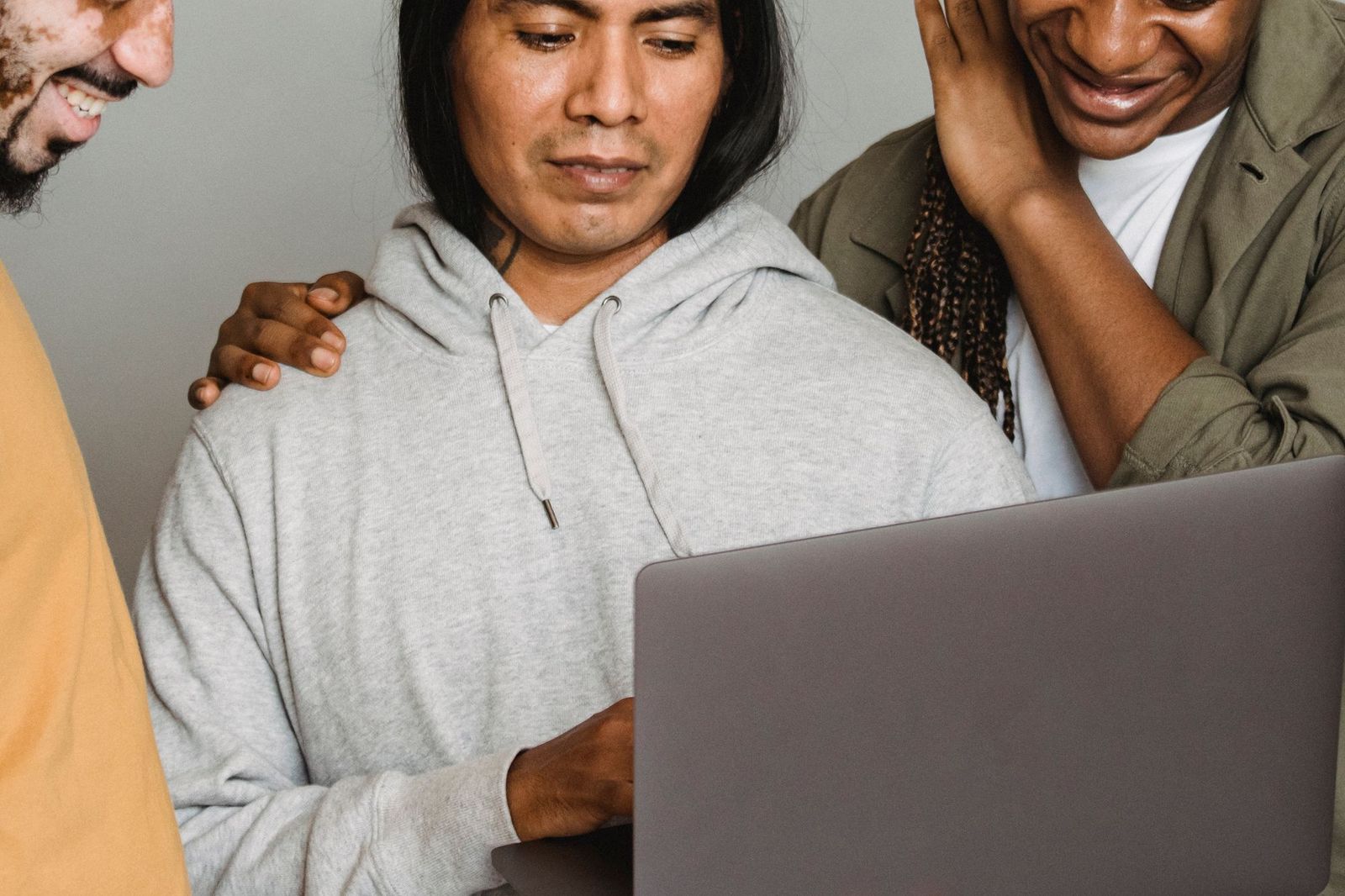 Three people leaning in together over an open laptop, one typing while the other two look at the screen and smile