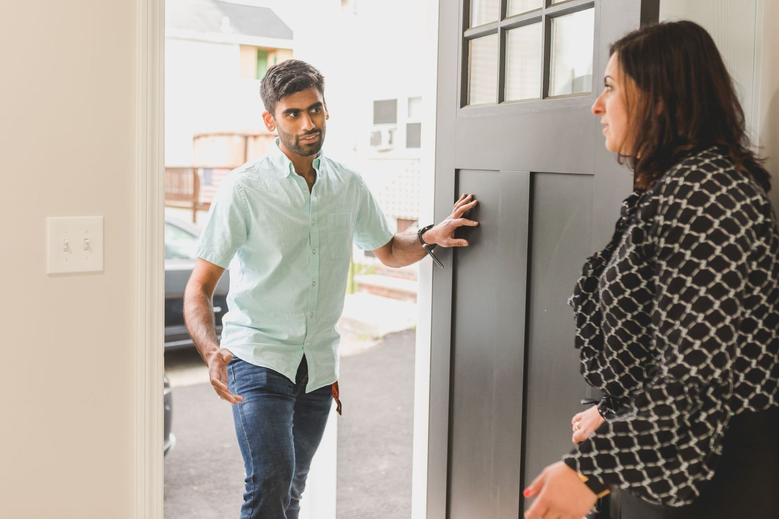A man standing in an open front doorway talking to a woman inside the house, one hand on the door as though about to leave