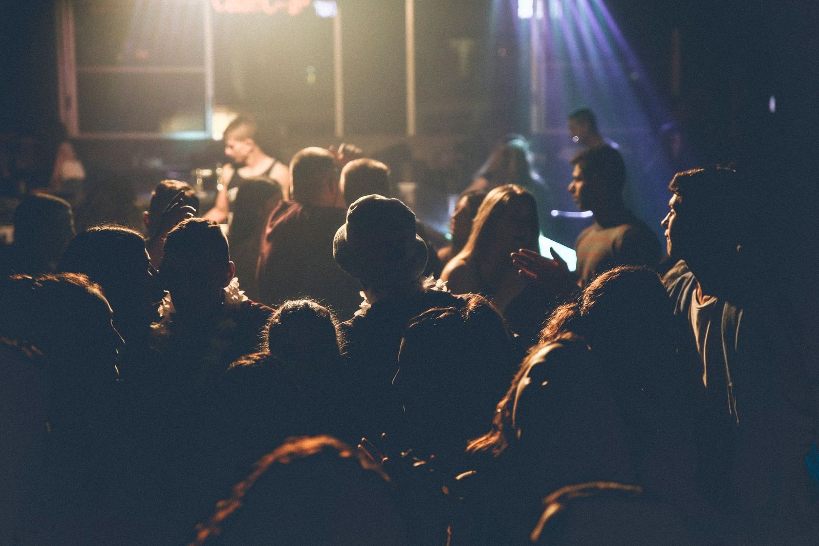 A large crowd of people silhouetted from behind at a live event, faces lit by stage lights and a beam of purple light across the room