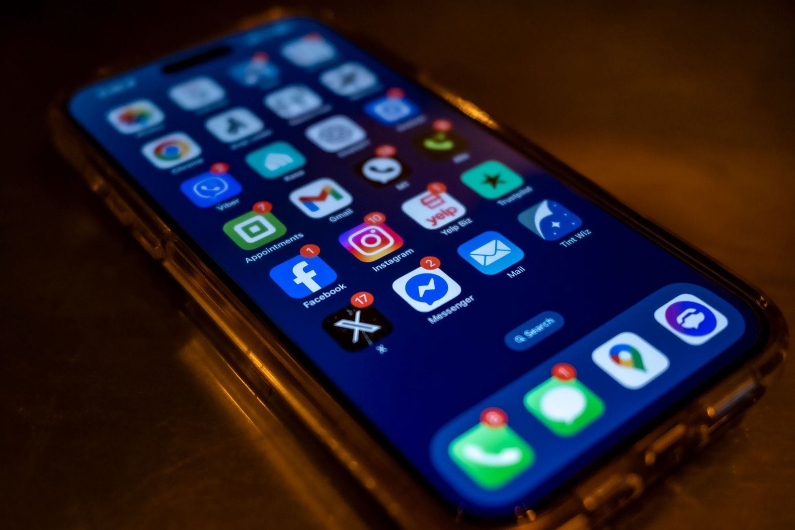 A phone lying on a dark table with its home screen lit up, showing rows of app icons including WhatsApp, Messenger and Instagram carrying unread notification badges