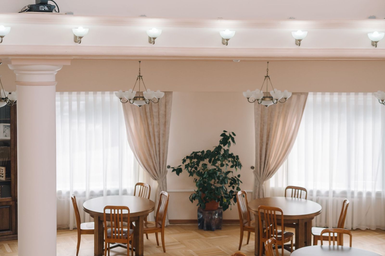 Rows of empty round tables set for a private function in a quiet function room with drawn curtains and chandeliers
