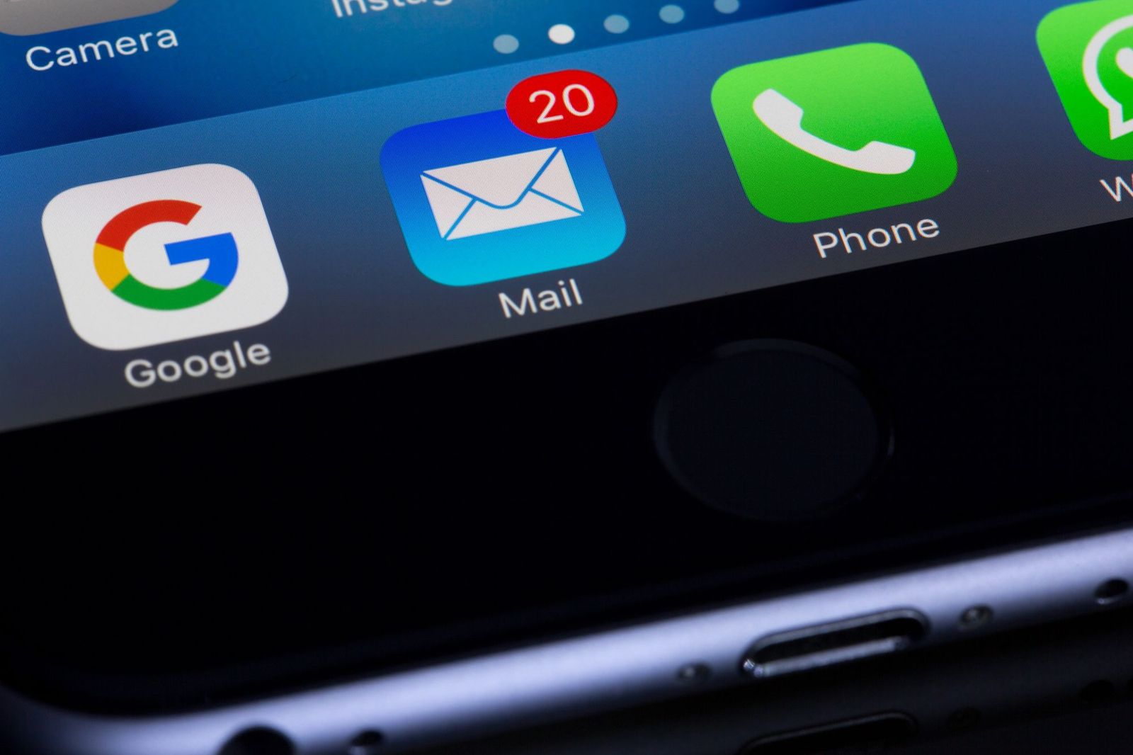 Extreme close-up of an iPhone home screen showing a Mail app icon with a red badge showing 20 unread notifications, next to Google, Phone and WhatsApp icons