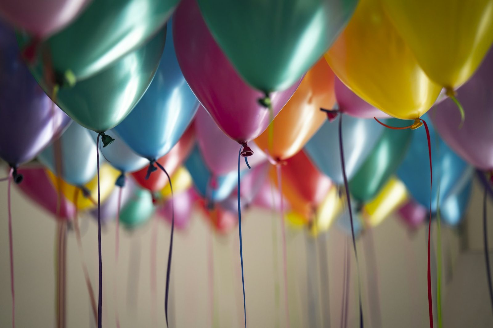 A cluster of colorful helium party balloons against a plain wall