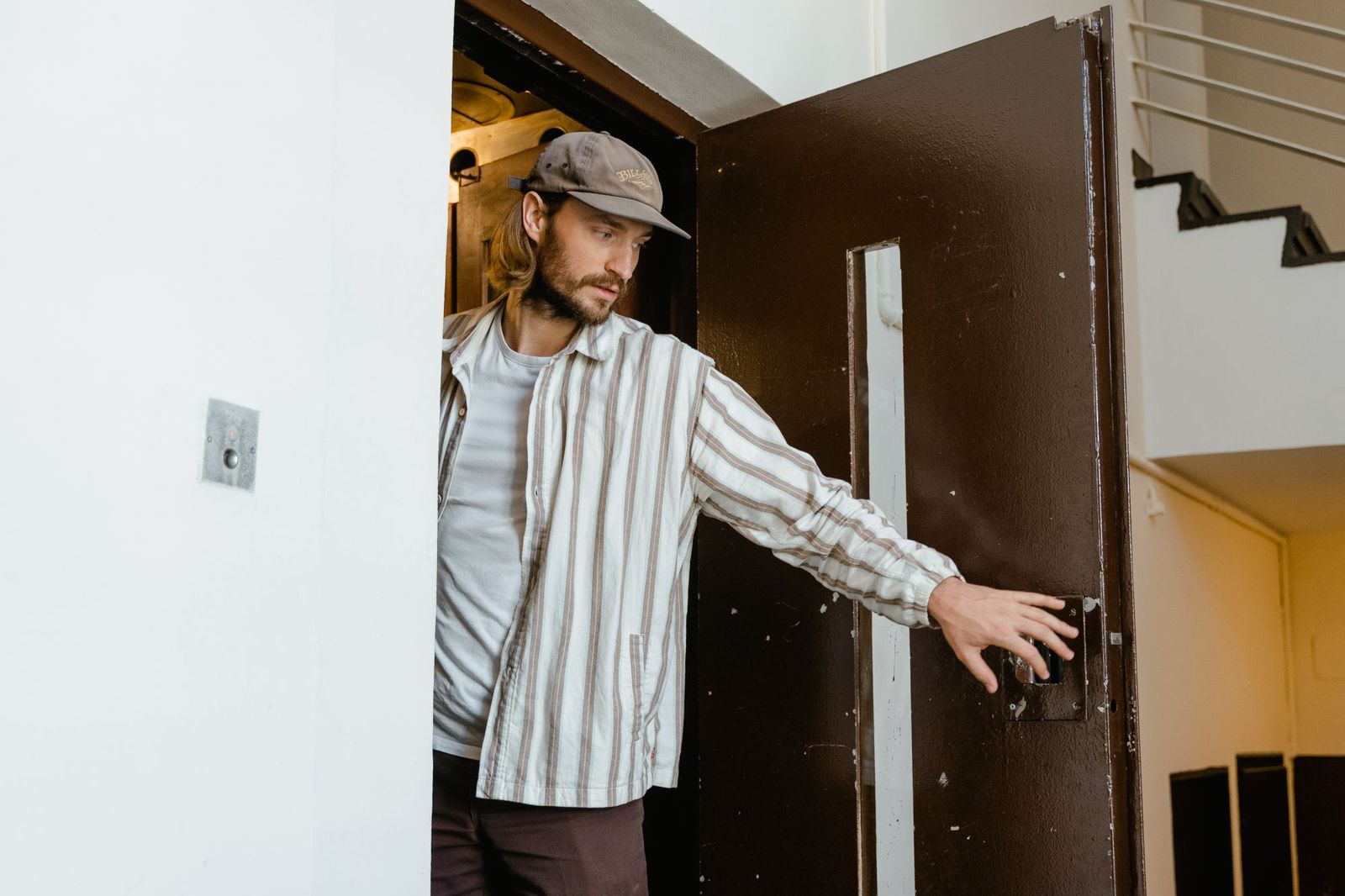 A man in a doorway reaching out to open a heavy dark door from the inside, with a stairwell visible behind him