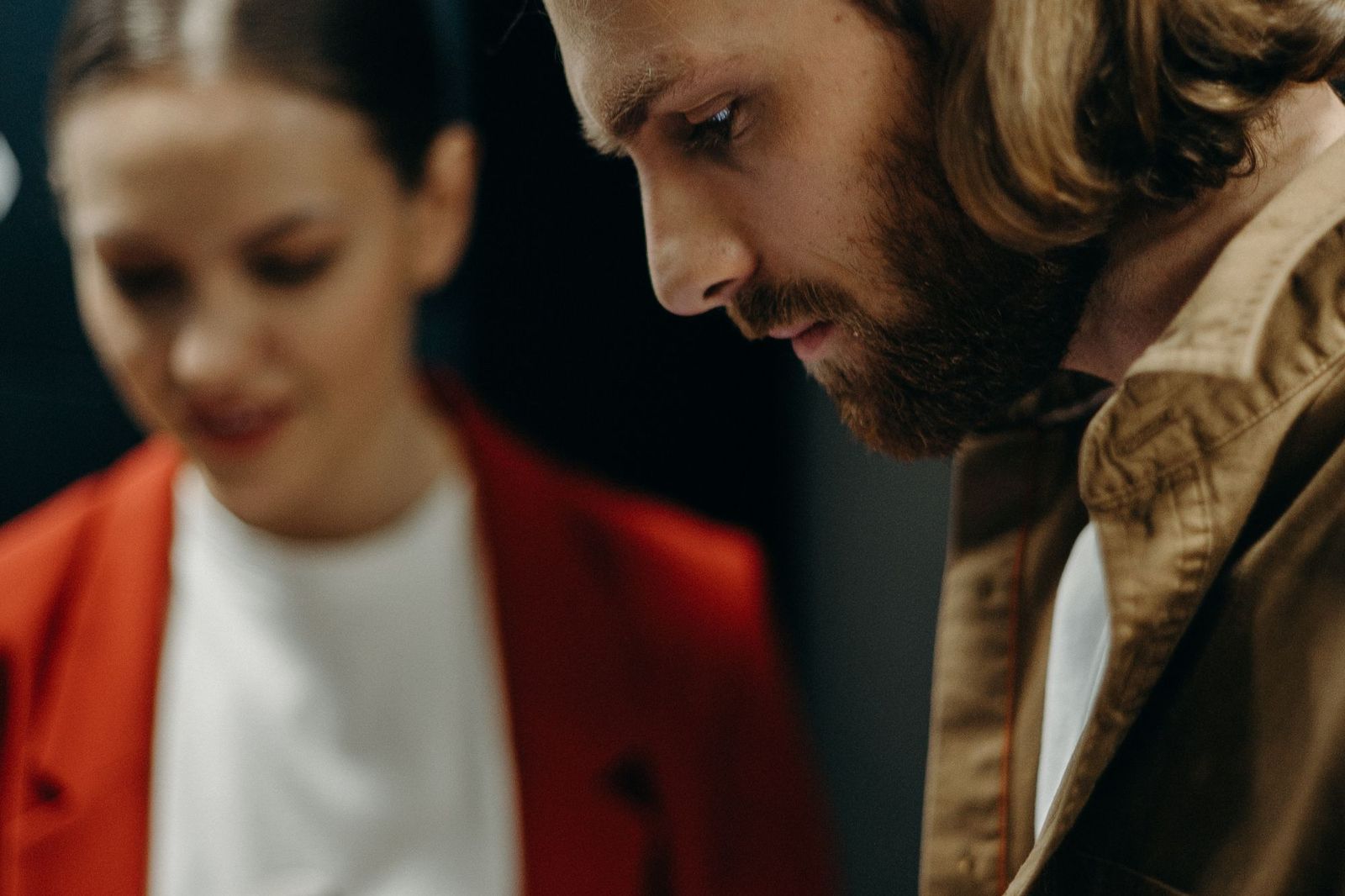 A man and a woman looking down and away from each other in a dim room, each absorbed in their own thought