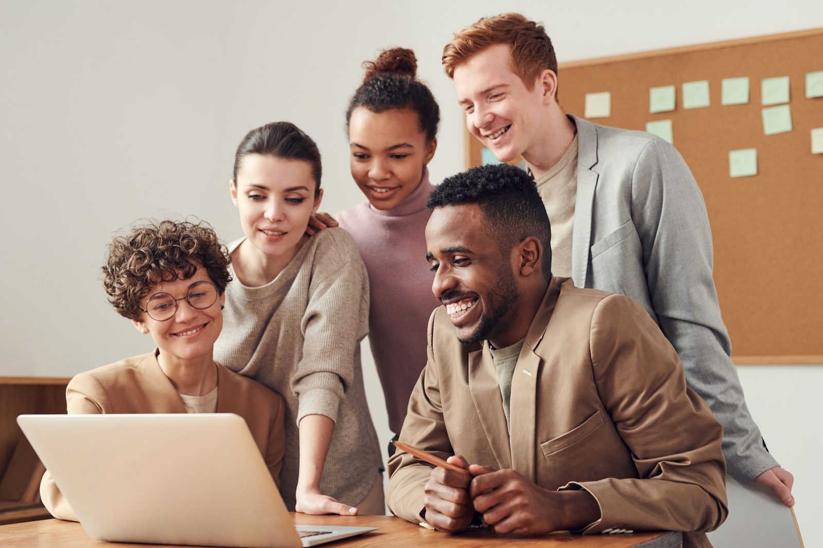 A group of colleagues gathered around a laptop together, smiling at something on the screen