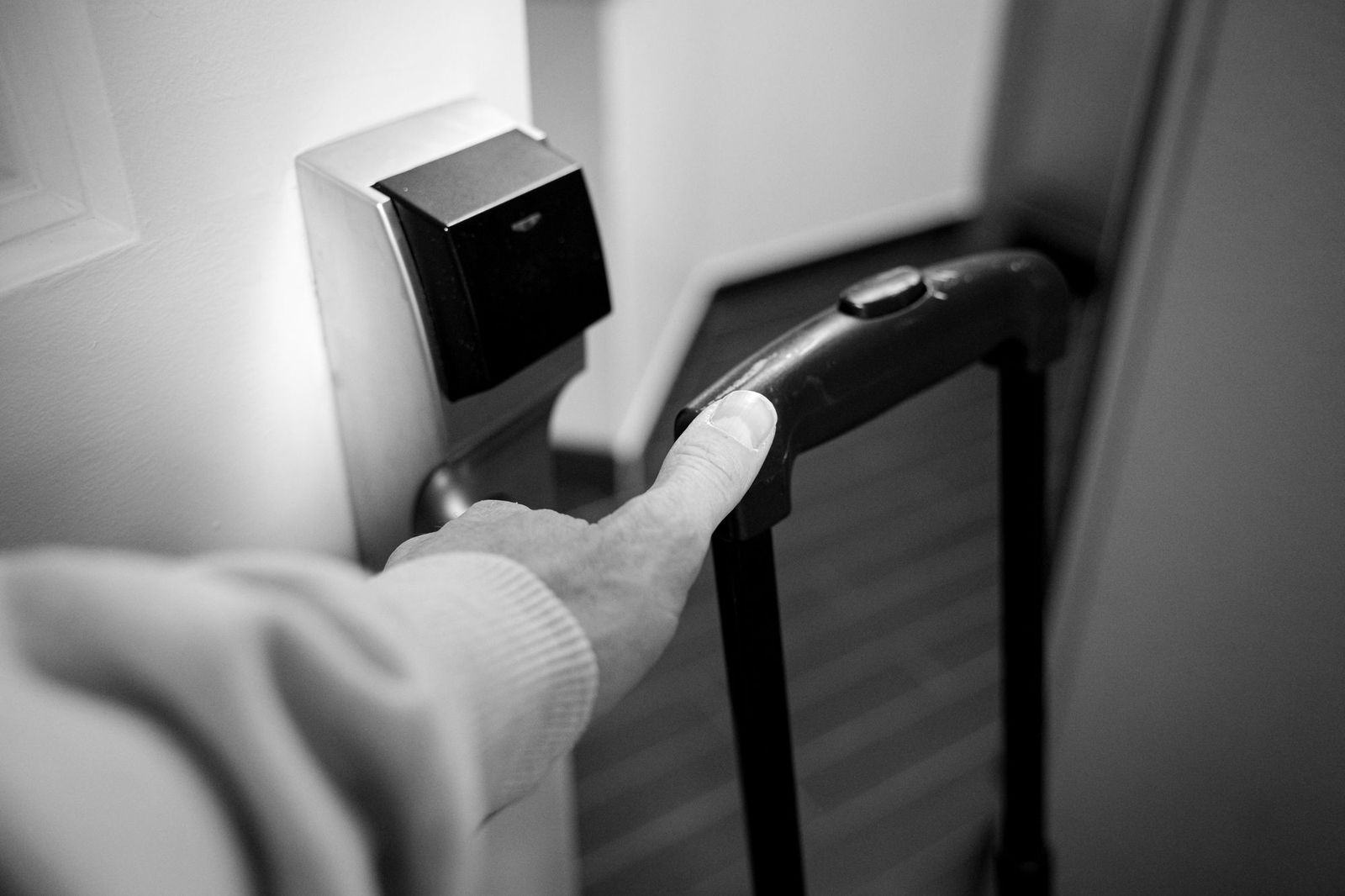 A person in a grey sweatshirt reaching for the handle of a wooden door in a lit corridor, a wristwatch visible on their arm