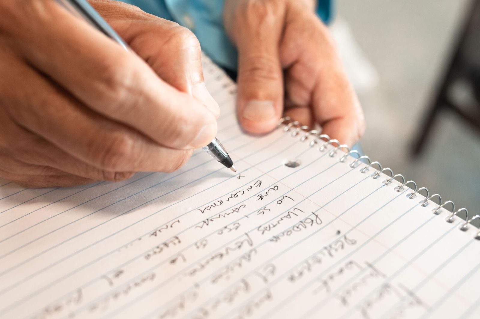 A close-up of a hand writing a handwritten list on a spiral notebook with a pen