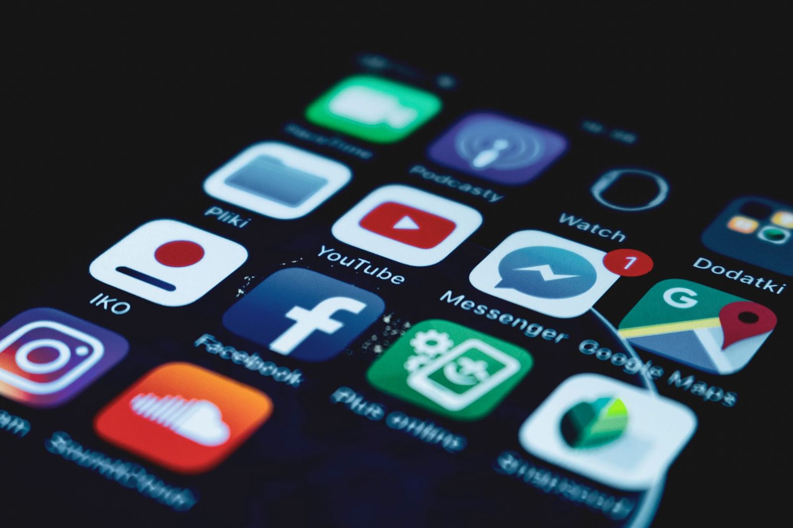 A close-up of a smartphone home screen at an angle, showing app icons including Messenger, Facebook, YouTube and Google Maps