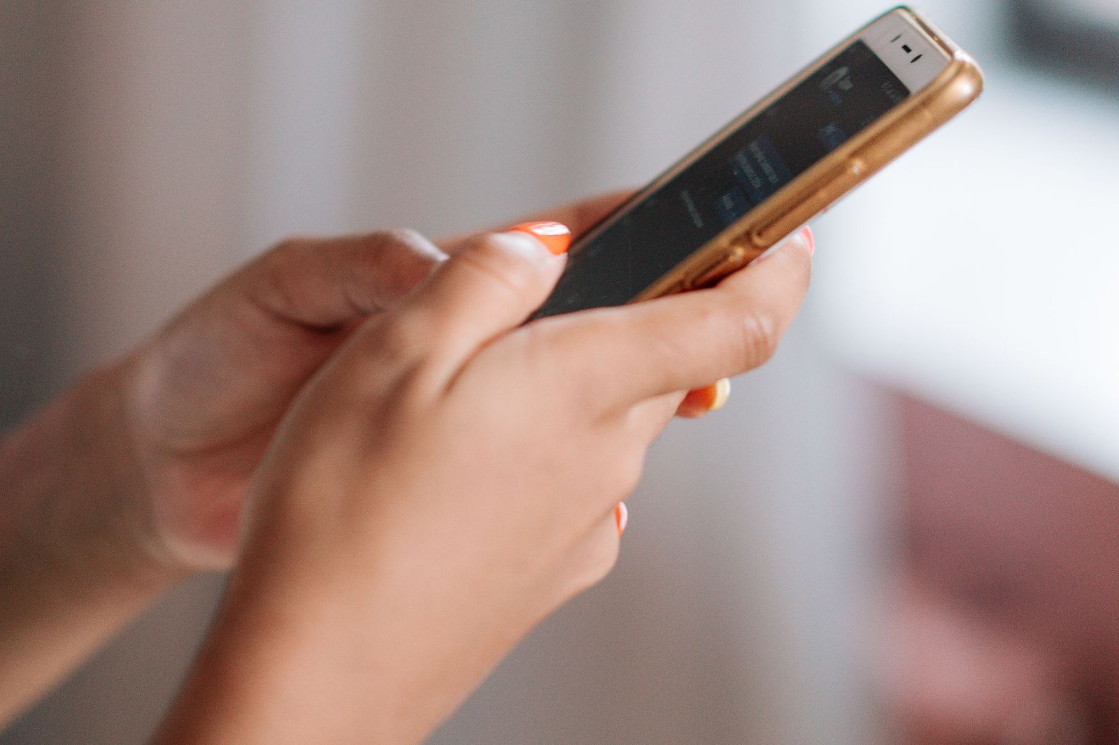 A hand holding a smartphone displaying a messaging app conversation, the person's nails painted orange