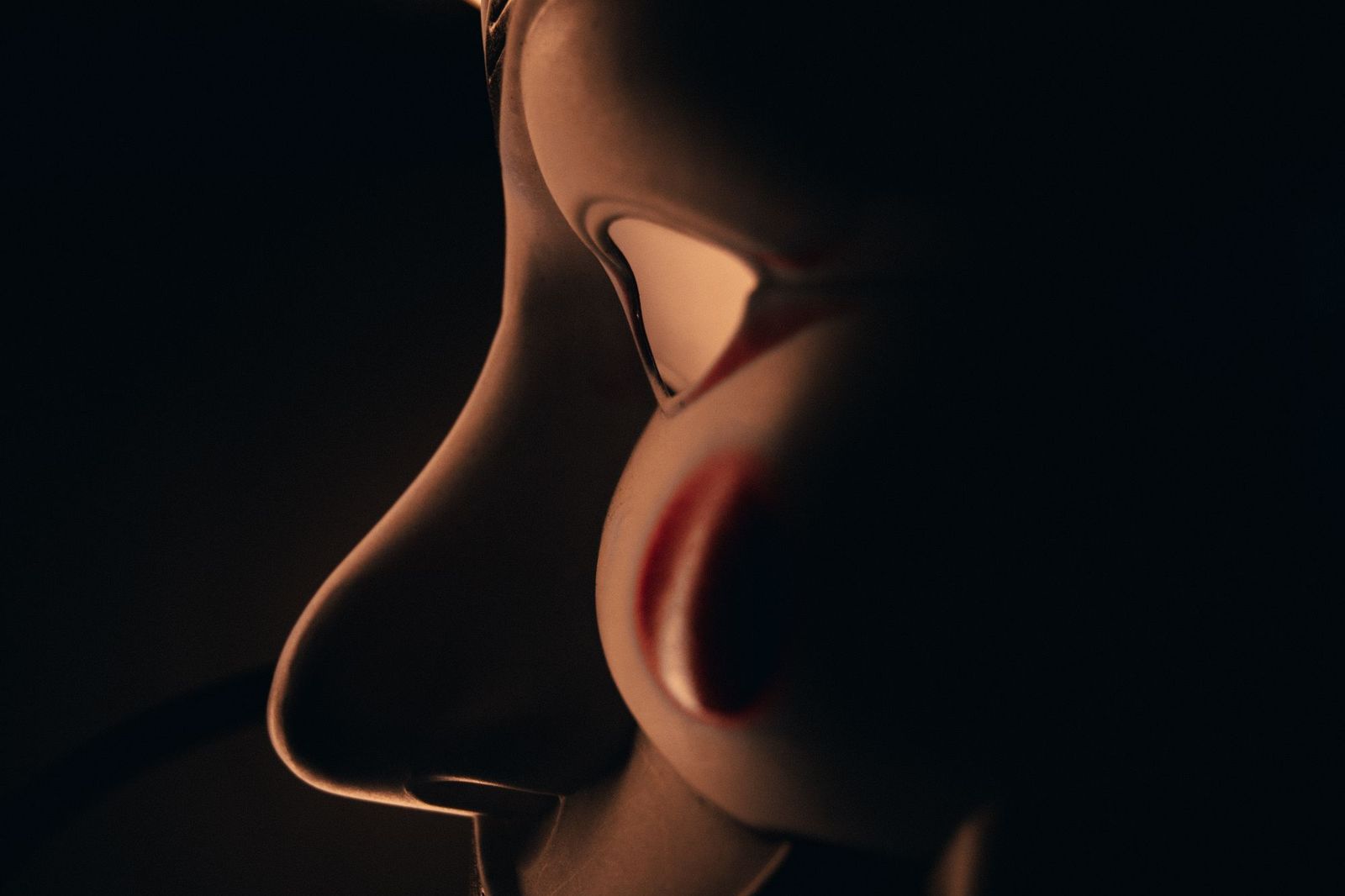 An extreme close-up profile photograph of a face lit warmly from one side against total darkness, features barely distinguishable