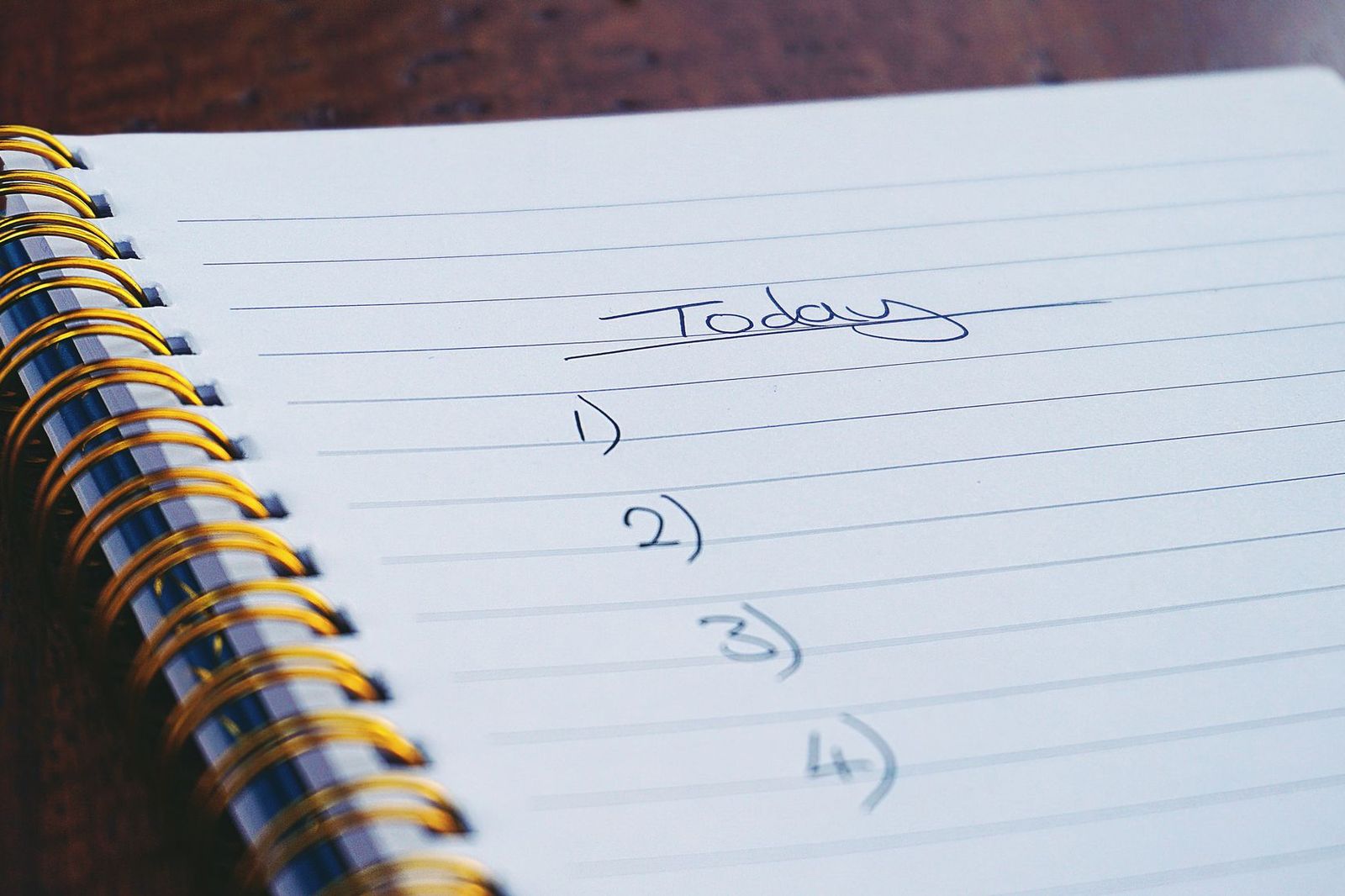 An open spiral notebook on a dark wooden table with the word Today handwritten and underlined, above a numbered list of four empty lines