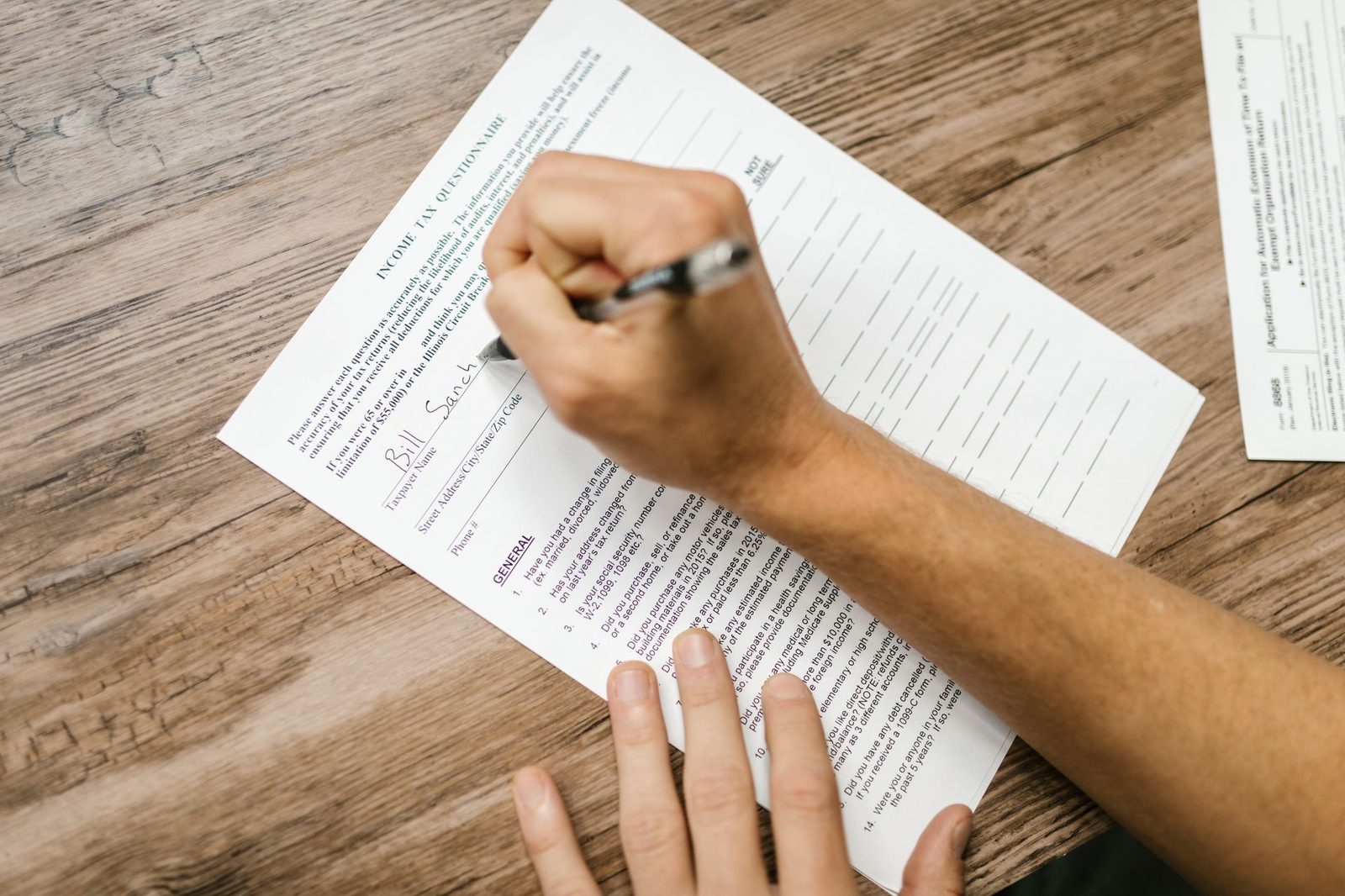 A person filling out a paper questionnaire on a clipboard at a table