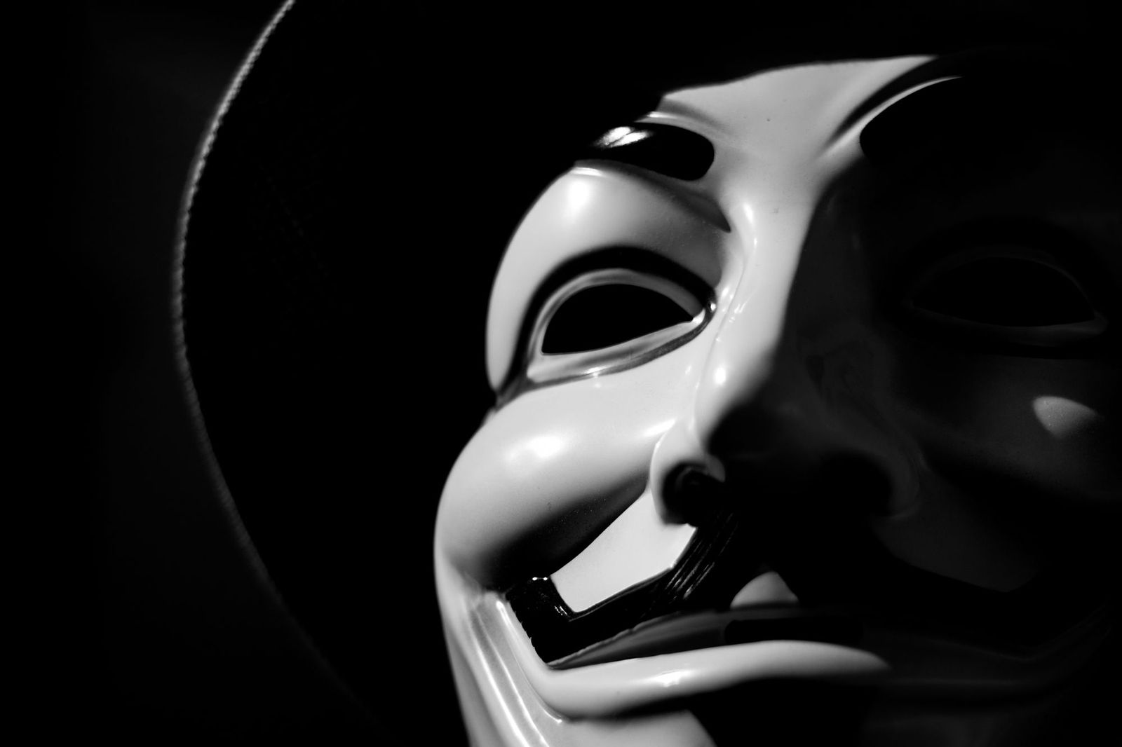 Close-up of a glossy white stylised mask, one eye visible, half the face lit and half in deep shadow against black