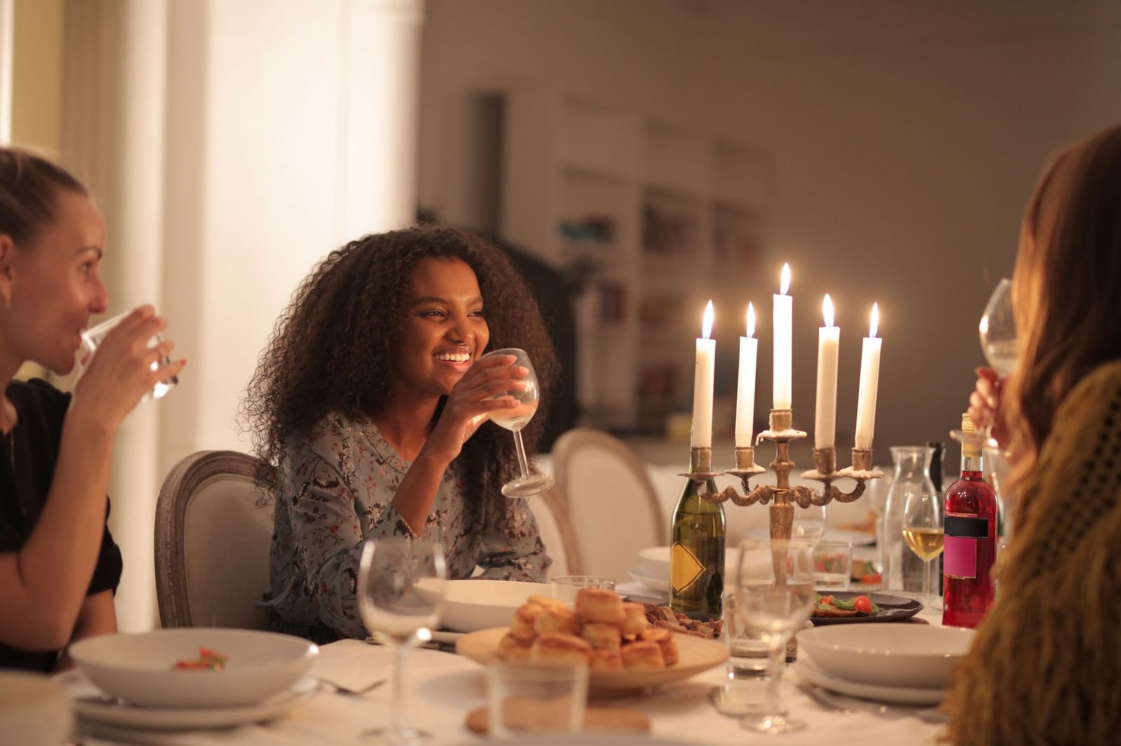 Guests sitting around a candlelit dinner table at night, talking and drinking wine, with bread and dishes laid out between them