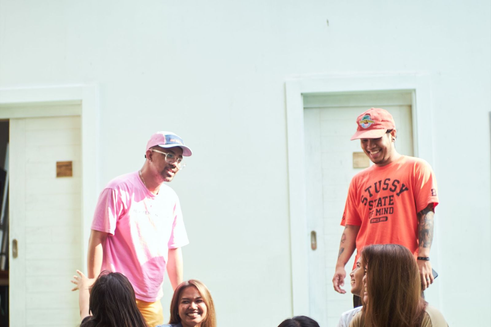 Two men laughing with a small group of friends gathered outside a house on a sunny day