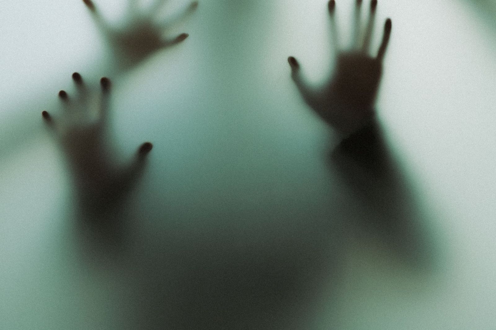 A blurred silhouette of two hands pressed against frosted glass from the other side, faint outlines of fingers visible