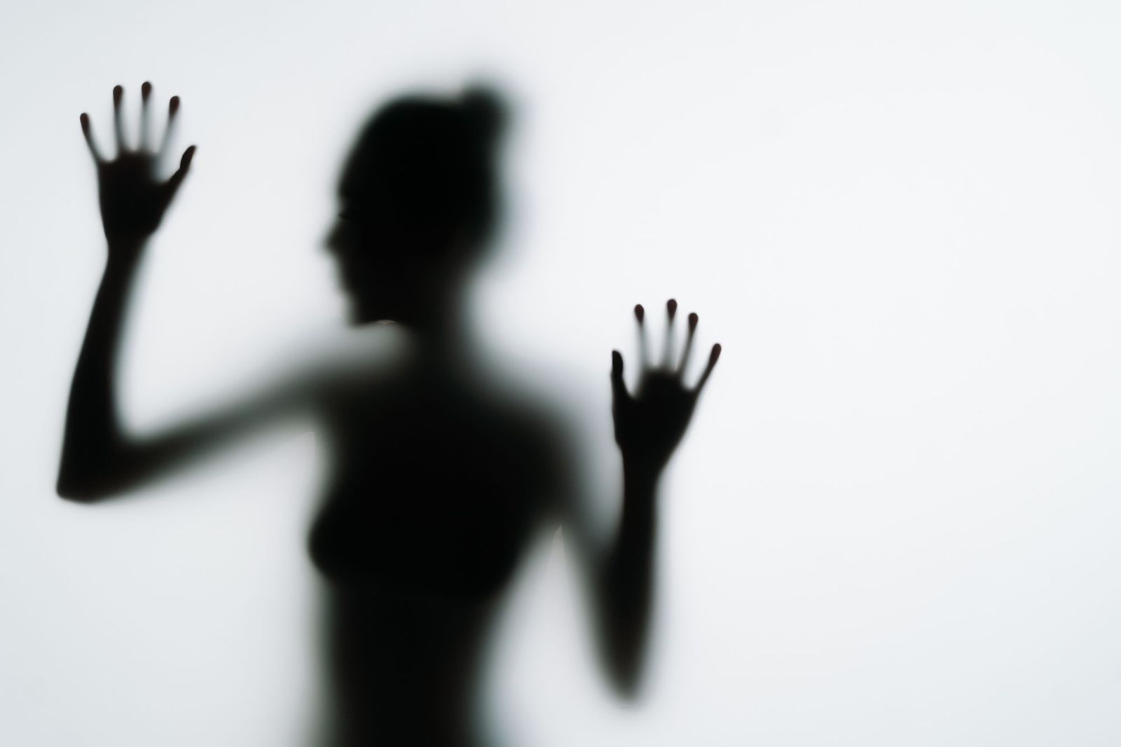A blurred silhouette of a person behind frosted glass, hands pressed flat against the surface
