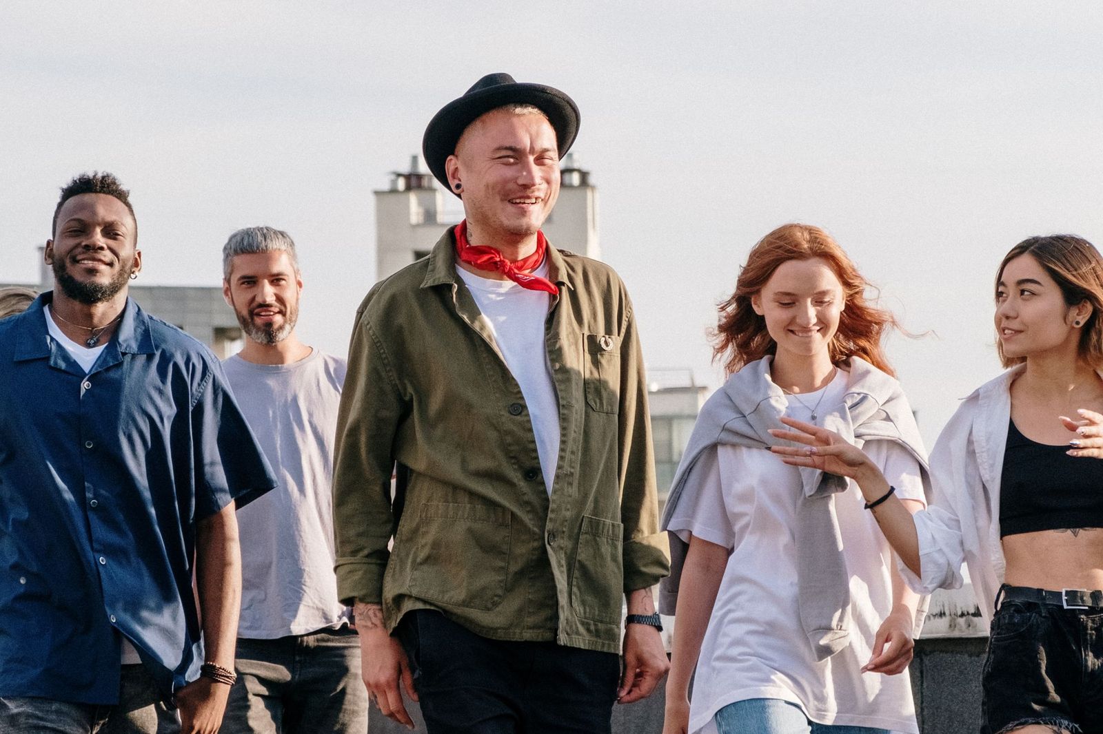 Five friends walking side by side along a rooftop in bright daylight, laughing and talking