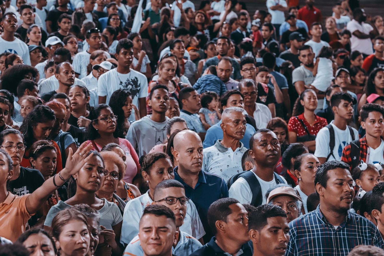 A very large crowd of people packed tightly together outdoors, many in white t-shirts and caps, photographed from above
