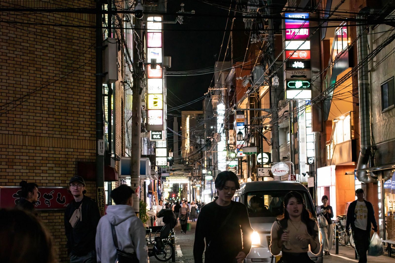 A crowded neon-lit pedestrian street at night with dozens of people crossing in different directions under illuminated signs