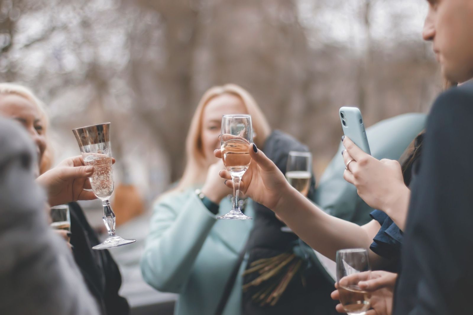 People outdoors raising glasses of sparkling wine together, one of them holding up a phone in a pale blue case