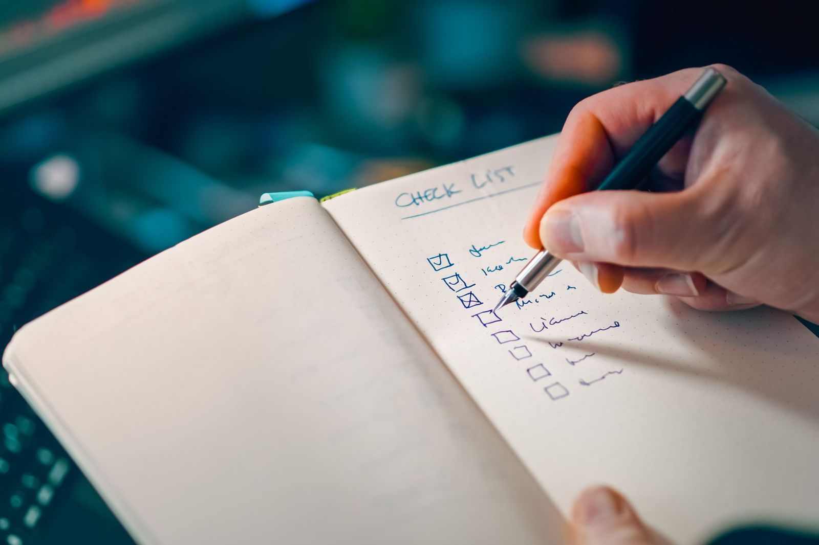 A hand writing a checklist in a dotted notebook with a fountain pen, several boxes already ticked and more still empty