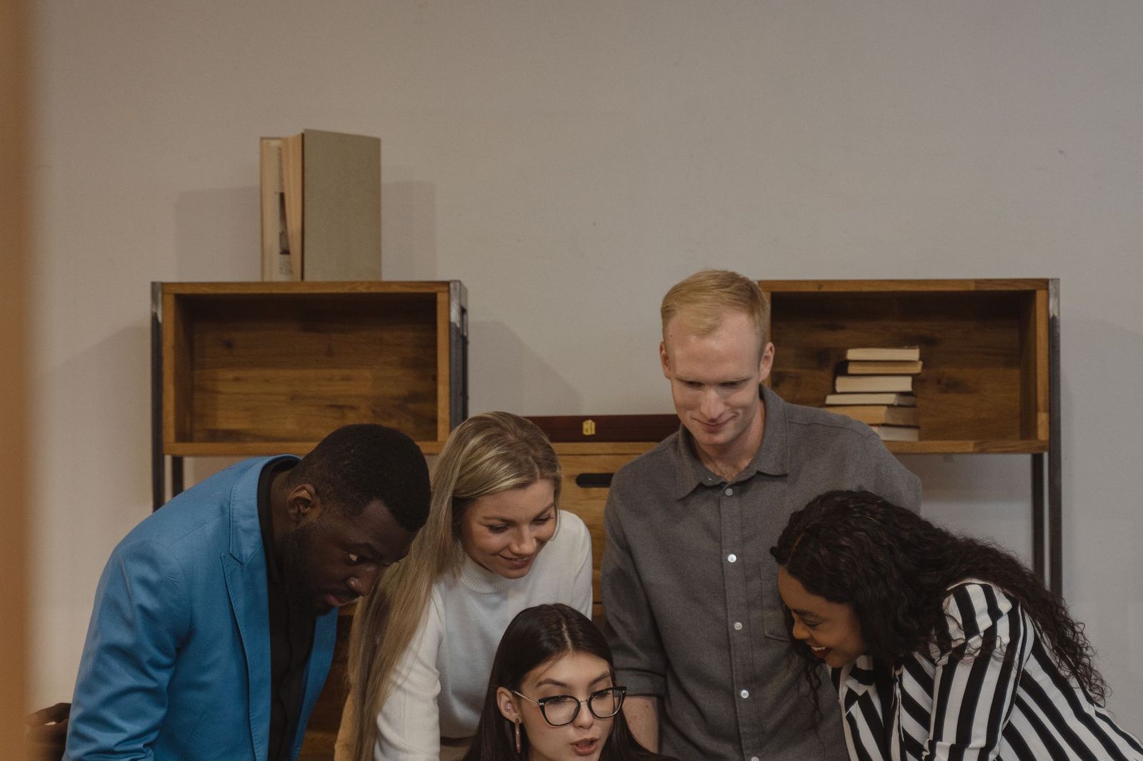 Five friends leaning in together over a laptop, smiling as they look at something on the screen
